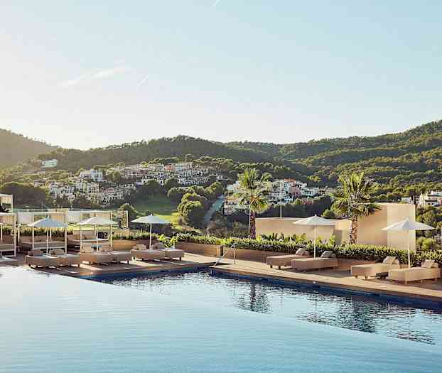 En utsikt fra et hotellområde med et basseng omgitt av solsenger, parasoller og et frodig landskap i bakgrunnen. (AI-generert tekst)