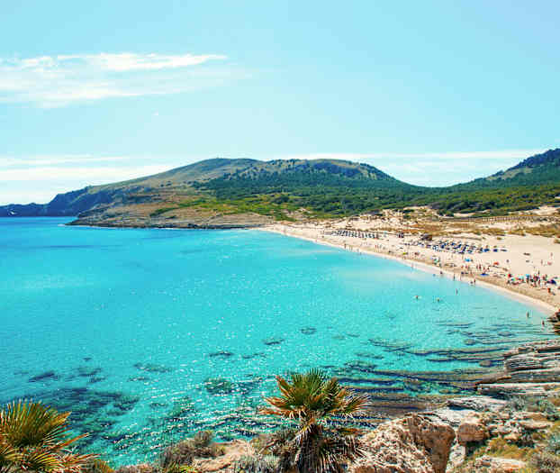 En sandstrand med turkisblått vann og grønne åser i bakgrunnen. (AI-generert tekst)