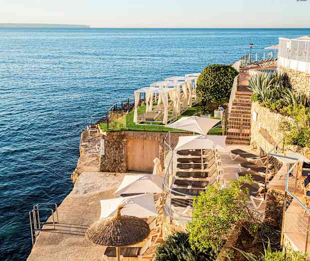 Utsikt over et klippeavsats ved havet med solsenger, parasoller og grøntområder. (AI-generert tekst)