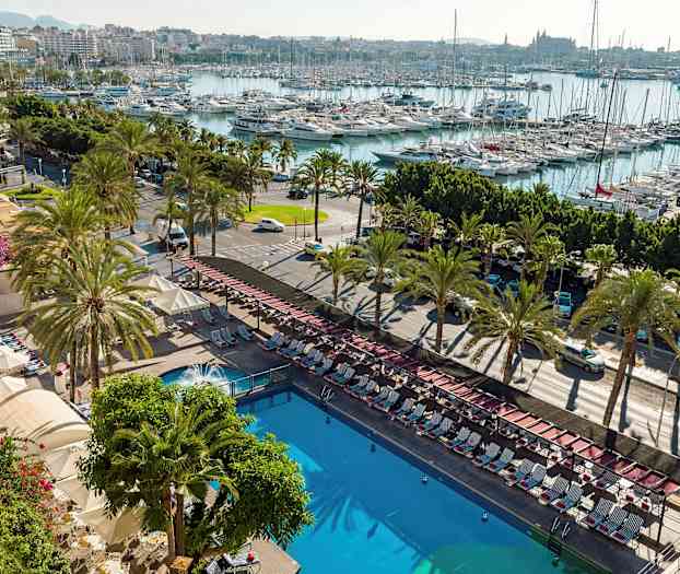 Utsikt over et utendørsbasseng omgitt av solsenger og parasoller, med en gate kantet av palmer og en marina full av båter i bakgrunnen. (AI-generert tekst)