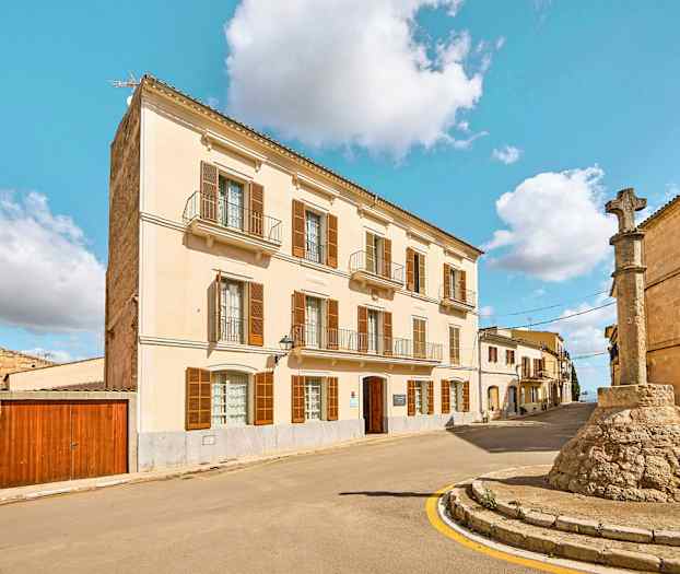 Gate med en bygning med lys fasade og en steinsøyle med kors. (AI-generert tekst)