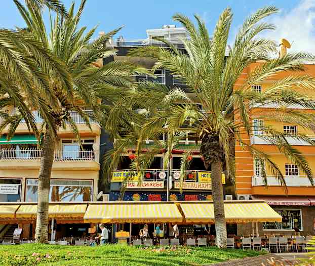 En bygning med restauranter og butikker samt palmer foran. (AI-generert tekst)