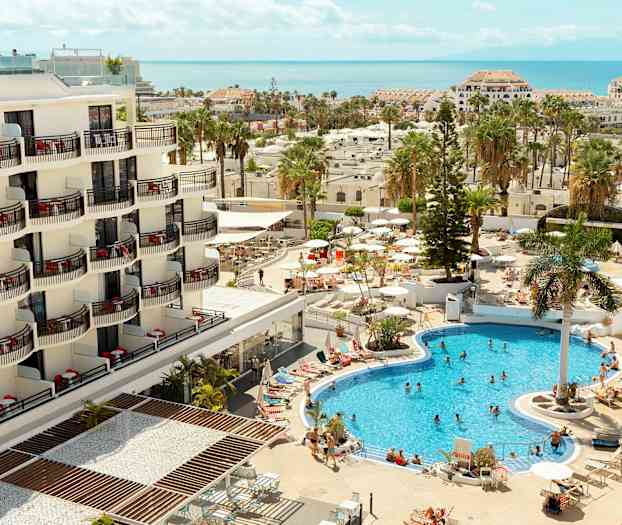 Et hotell med balkonger og et bassengområde med gjester og parasoller. (AI-generert tekst)