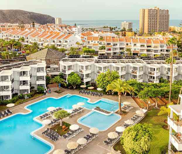 Utsikt over hotellområdet med bassenger, bygninger og omkringliggende landskap. (AI-generert tekst)