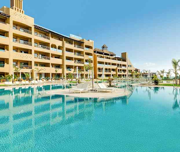 Hotellets utendørsbasseng med solsenger og omkringliggende bygninger. (AI-generert tekst)