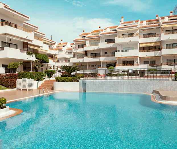 Hvit bygning med terrasser og et turkis basseng i forgrunnen. (AI-generert tekst)