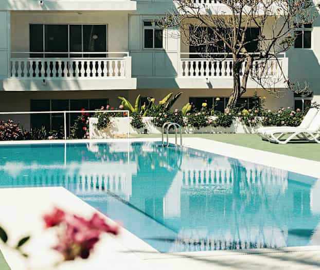 Utendørs svømmebasseng med solsenger ved et hvitmalt hotell. (AI-generert tekst)