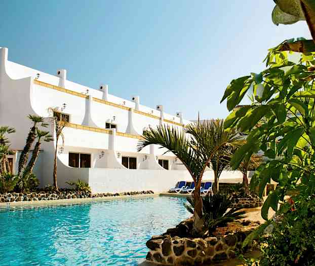 Hvit bygning med palmer ved et basseng. (AI-generert tekst)