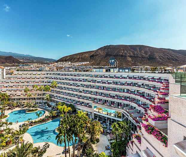 Bilde av hotellkompleks med bassengområde og omkringliggende fjell. (AI-generert tekst)