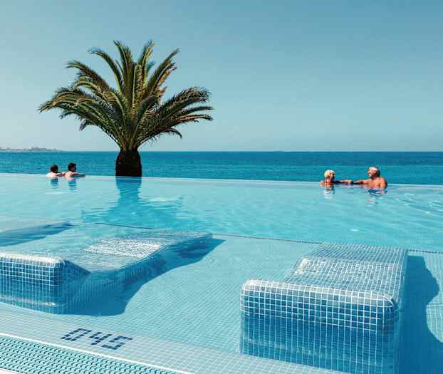 Et infinitybasseng med utsikt over havet, med en palme i midten og gjester som svømmer. (AI-generert tekst)