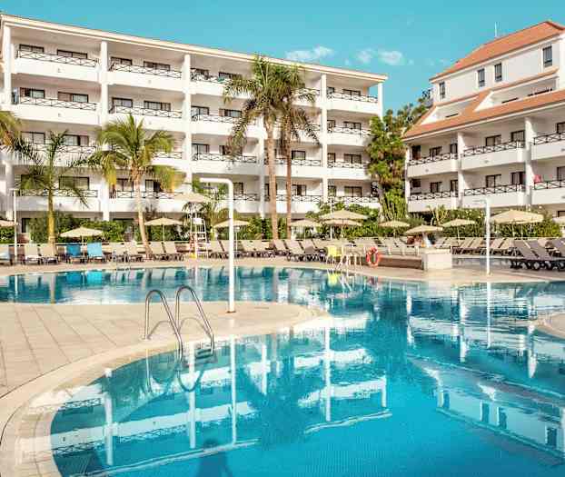 Bilde av et hotellkompleks med hvite bygninger, trær og et basseng. (AI-generert tekst)