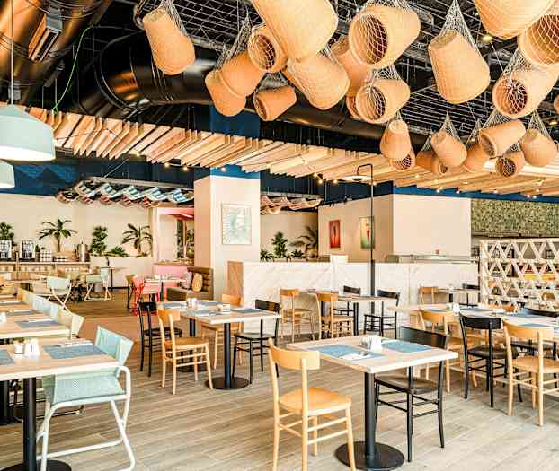 En lys og moderne restaurant med trebord, ulike typer stoler, planter og dekorative objekter i taket. (AI-generert tekst)