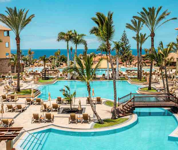 Hotellbassengområde med solsenger, palmer og havutsikt. (AI-generert tekst)