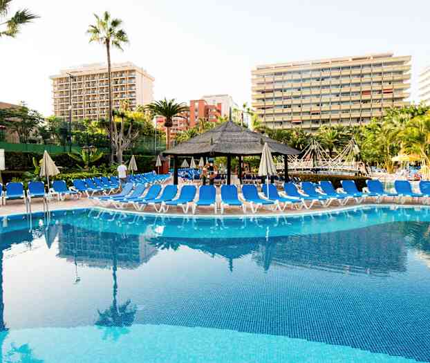 Et basseng med solsenger rundt og hotellbygninger i bakgrunnen. (AI-generert tekst)