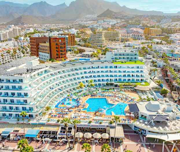 Utsikt over et feriested med bassenger og omkringliggende bygninger i et fjellområde. (AI-generert tekst)