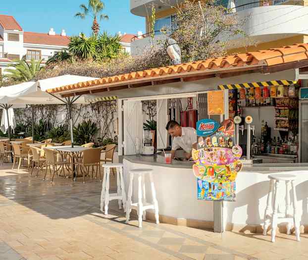 En uteservering med bord og parasoller ved siden av en bar. (AI-generert tekst)