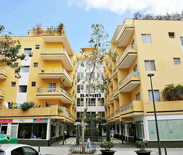 Gul bygning med balkonger og butikker i første etasje. (AI-generert tekst)