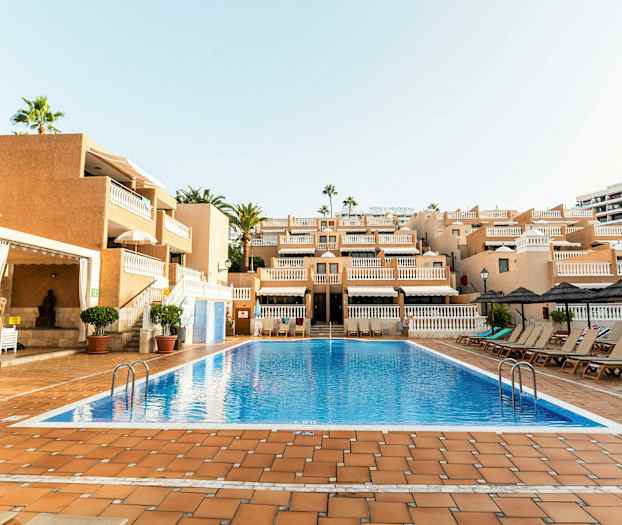 Et utendørs svømmebasseng foran en bygning med flere etasjer og balkonger. (AI-generert tekst)