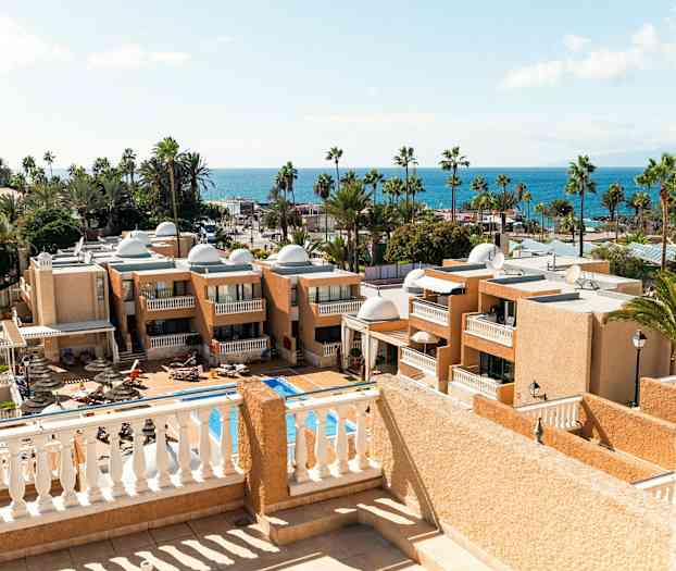 Utsikt over hotellbygninger og et basseng med havet i bakgrunnen. (AI-generert tekst)