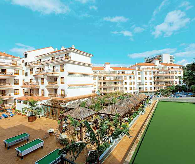 Flere hvitmalte bygninger med røde tak omgitt av en stor indre gårdsplass med basseng og sitteplasser. (AI-generert tekst)