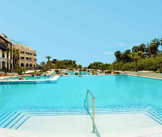 Stor svømmebasseng ved et hotell med omkringliggende grøntområder. (AI-generert tekst)