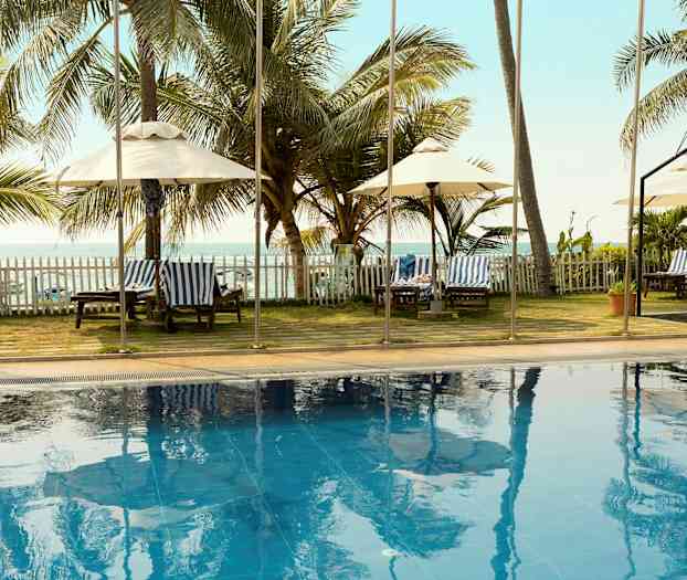 Et utendørs basseng med palmer og solsenger i bakgrunnen, samt havutsikt. (AI-generert tekst)