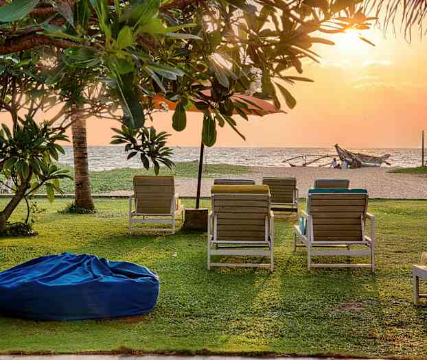 En plen på en strand med solstoler og trær under en solnedgang. (AI-generert tekst)