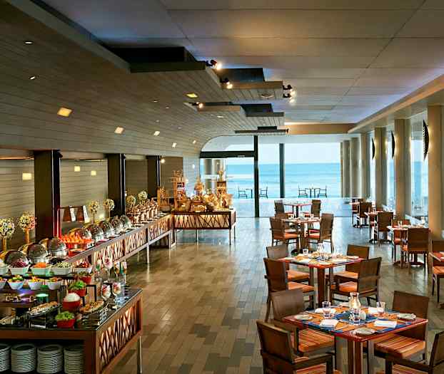 Bilde av en restaurant med dekkede bord og en buffé med ulike retter, samt store vinduer som vender ut mot havet. (AI-generert tekst)