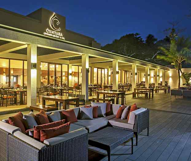 En utendørsterrasse ved en restaurant med bord, stoler og sofagrupper i skumringslys. (AI-generert tekst)