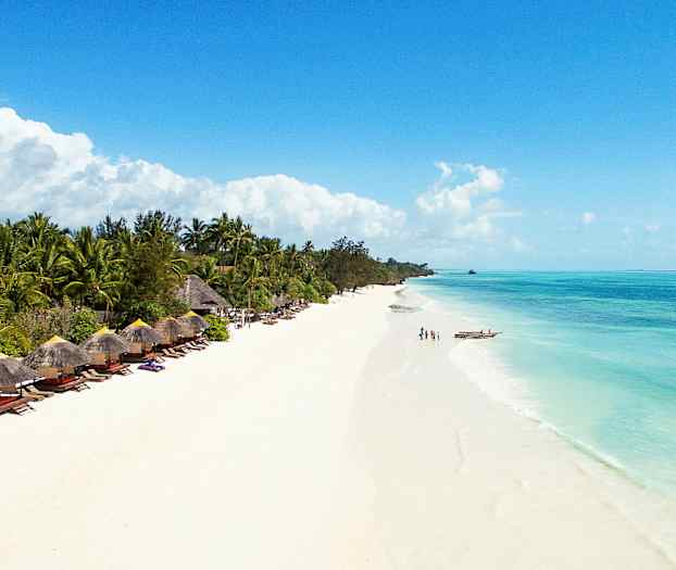 En strand med hvit sand og klart blått vann, omgitt av frodige palmer og parasollstoler. (AI-generert tekst)