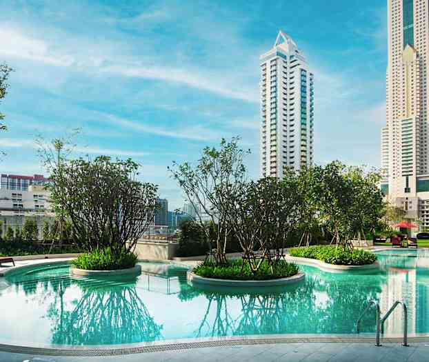 Et basseng med klart blått vann omgitt av grøntområder og høye bygninger i bakgrunnen. (AI-generert tekst)