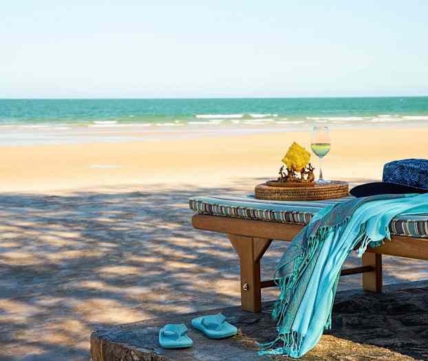 Solstol med en hatt, håndkle og flip-flop-sandaler ved stranden. (AI-generert tekst)