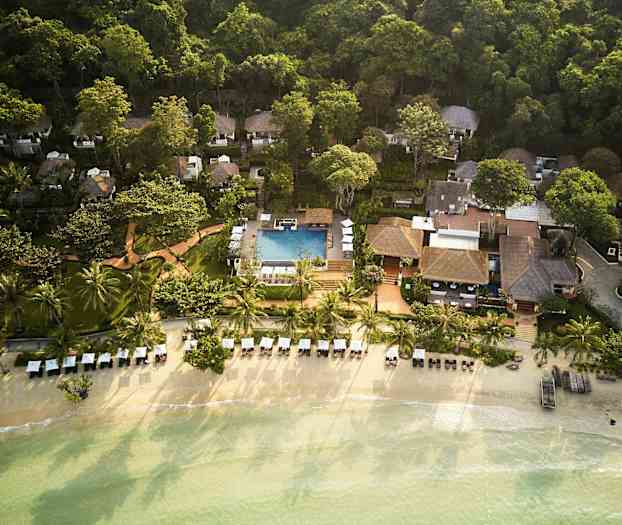 Flyfoto av et ferieanlegg ved stranden med palmer, solsenger og et basseng, omgitt av frodig grøntområde. (AI-generert tekst)