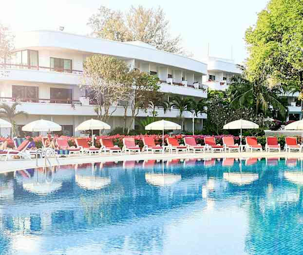 Bassengområde med solsenger og parasoller foran et hotell. (AI-generert tekst)