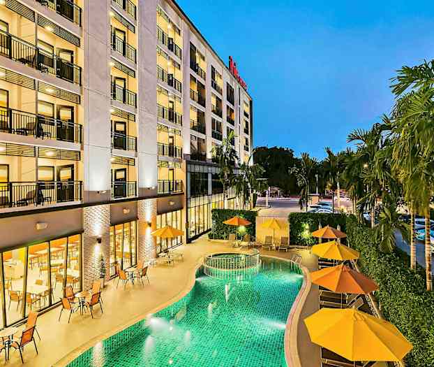 Bygning med flere etasjer, grønn basseng og parasoller ved siden av. (AI-generert tekst)