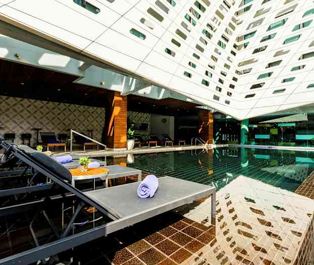 Et moderne utendørsområde med et basseng, solsenger og et tak dekket av geometriske åpninger. (AI-generert tekst)