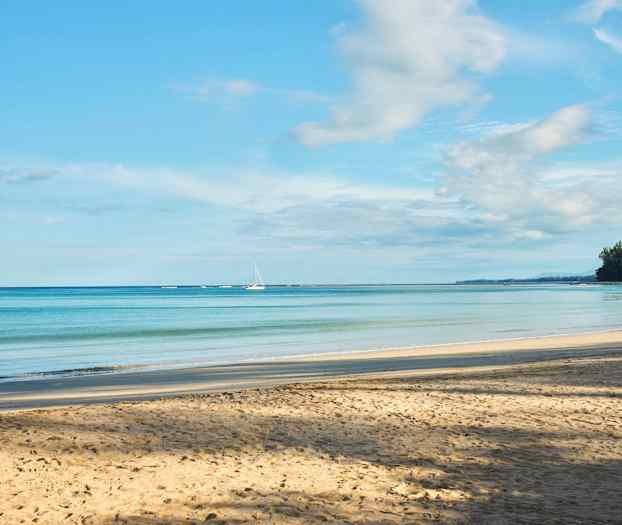 En sandstrand med en rolig havutsikt, to seilbåter ved horisonten og treforede kyster til høyre. (AI-generert tekst)