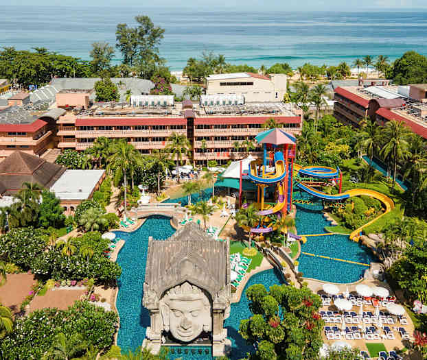 Utendørsområdet med vannpark, basseng og grøntområder foran bygninger ved sjøen. (AI-generert tekst)