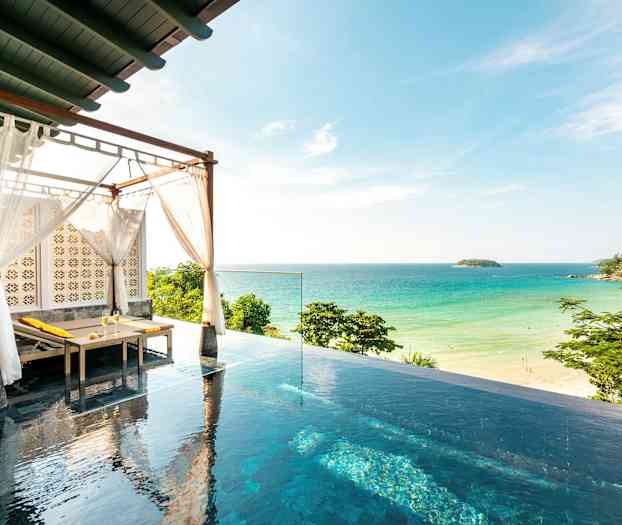 Bildet viser et infinitybasseng med en solseng under et tak med hvite tekstiler, og i bakgrunnen er en sandstrand og havet. (AI-generert tekst)