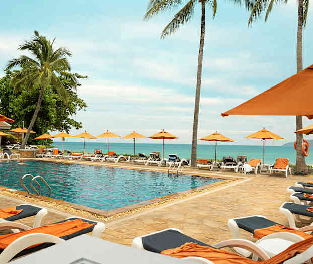 Utendørs basseng omgitt av solsenger og parasoller, med utsikt mot havet. (AI-generert tekst)