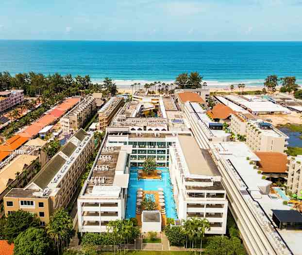 En hotellbygning med et basseng i midten, omgitt av flere bygninger nær havet. (AI-generert tekst)