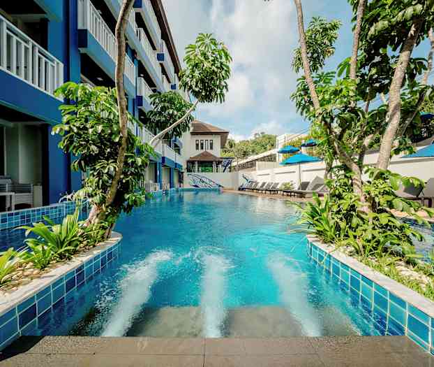 Et basseng med frodig vegetasjon omgitt av bygning og solsenger. (AI-generert tekst)