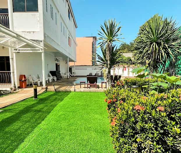 Et utendørsbilde av en bygning med en grønn plen og omgivende planter. (AI-generert tekst)