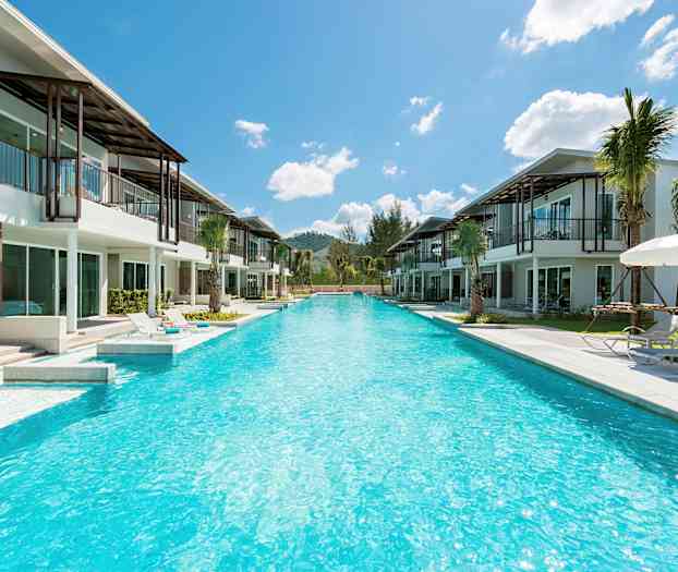 Utsikt over et langt basseng omgitt av moderne villaer og solsenger under parasoller. (AI-generert tekst)