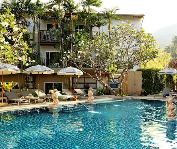 Bassengområde med parasoller og solsenger foran et hotell. (AI-generert tekst)