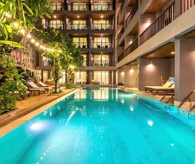 Et utendørsbasseng omgitt av solsenger og planter foran et moderne hotell. (AI-generert tekst)