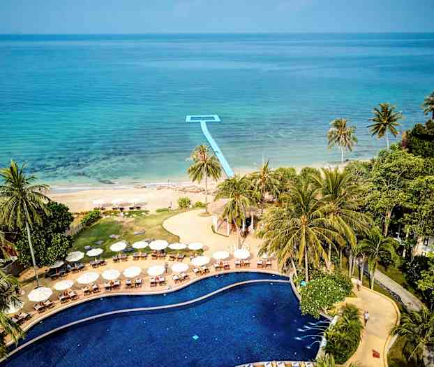 Bilde av et basseng omgitt av solsenger og parasoller, med utsikt mot en strand og havet. (AI-generert tekst)