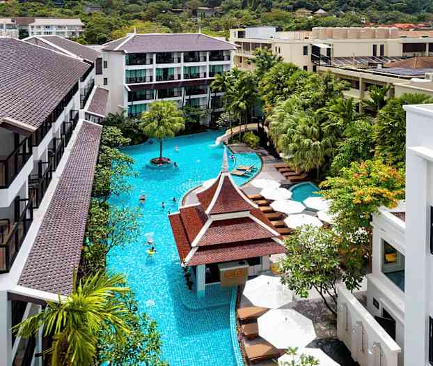 Lyst bilde av et hotellområde med et stort basseng, omgitt av grønne trær og bygninger med brune tak. (AI-generert tekst)