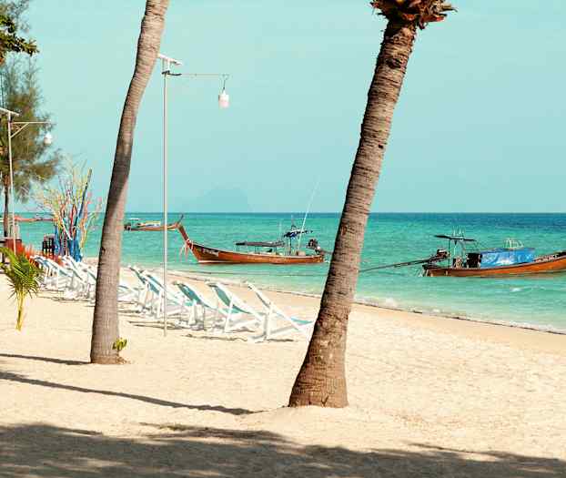 Strand med palmer, solsenger og tradisjonelle trebåter i havet. (AI-generert tekst)