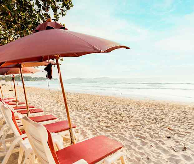 Strand med solsenger og parasoller på rad ved sjøen. (AI-generert tekst)